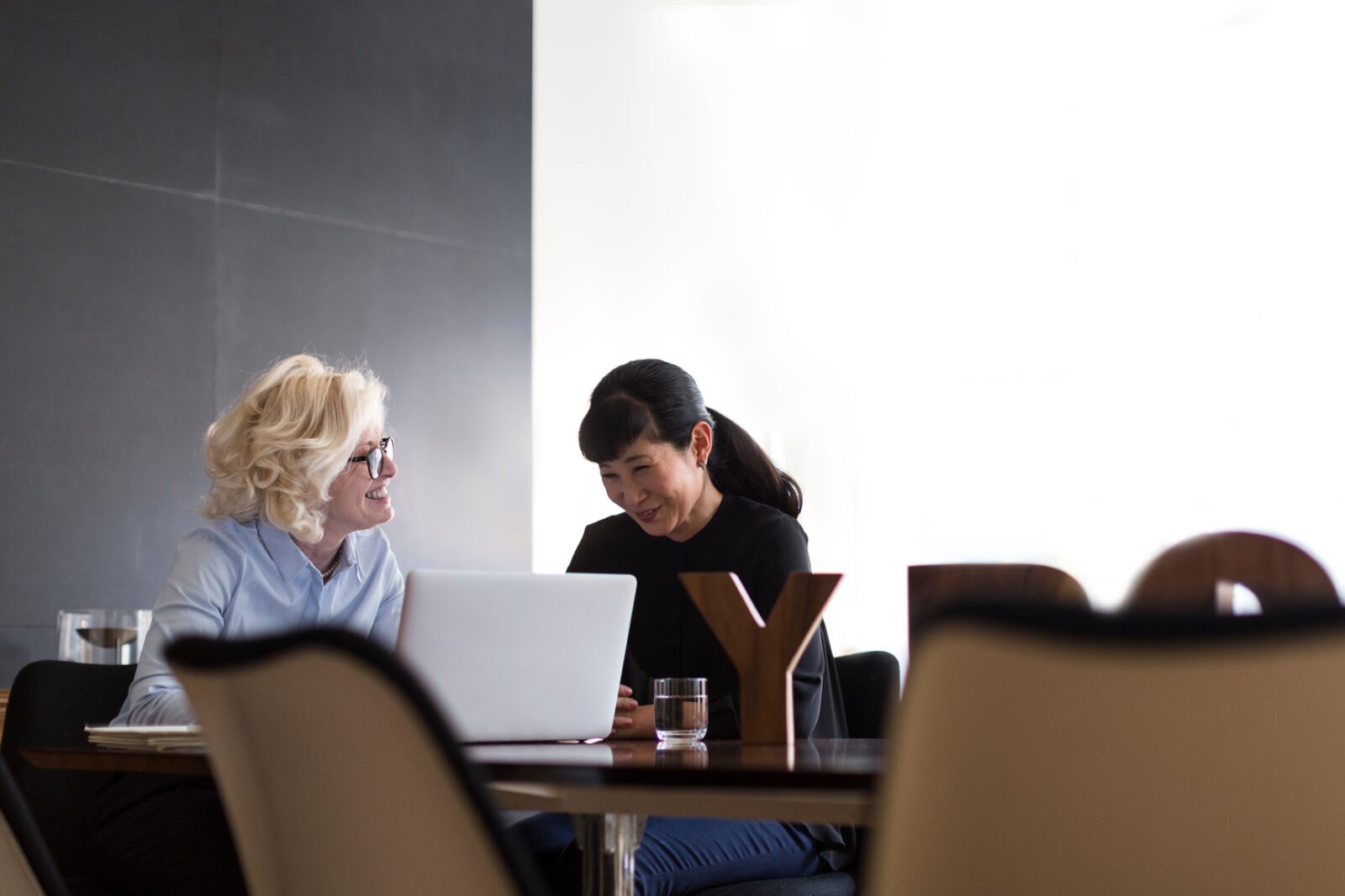 Cheerful businesswoman with smiling partner working on laptop and discussing ideas