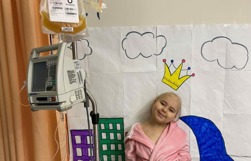 Young patient with cancer smiles while standing next to a bag of donated blood platelets in a hospital