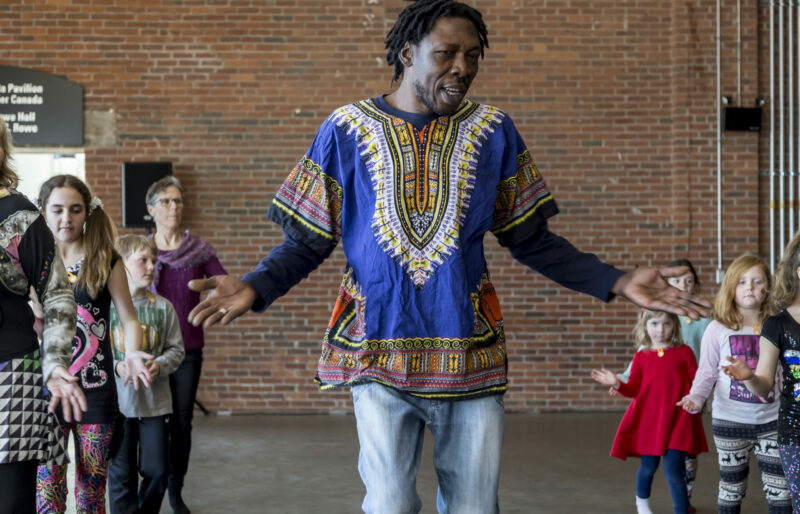 Children of all ages are dancing, lined up in two rows along side a dancer while they attentively follow instructions.