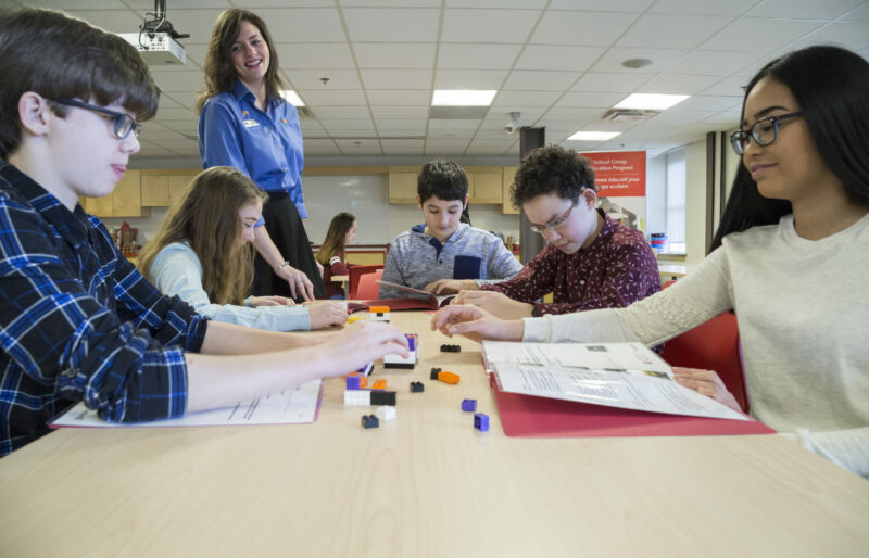 Students sit at a table in the Museum classroom facing each other as a Heritage Interpreter guides them through one of our education programs involving lego blocks.