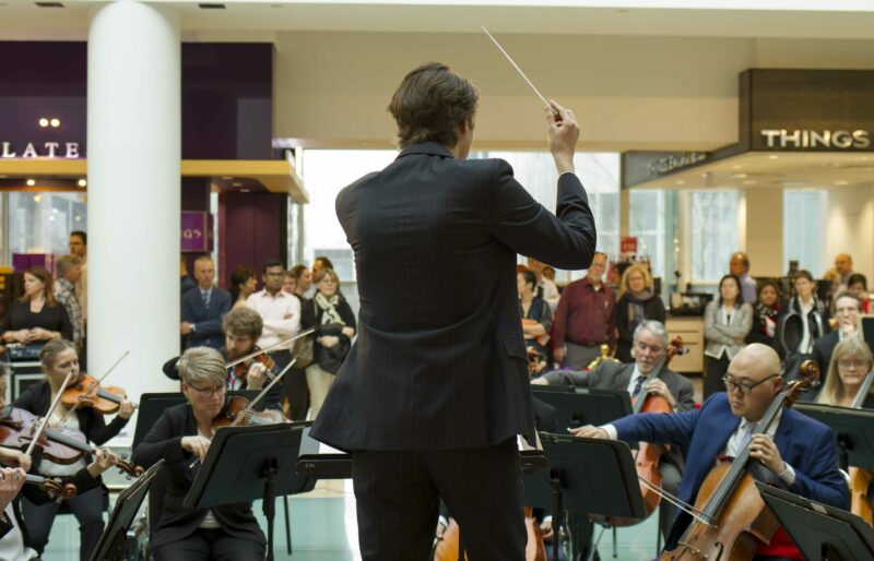 Associate conductor leads orchestra performance in lobby of public building