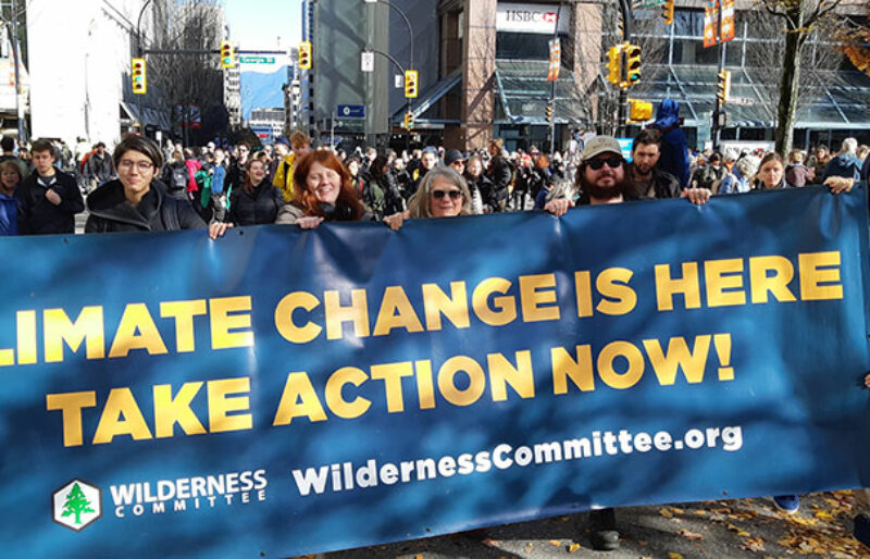 A crowd of people, with those in the fore holding a sign that says 