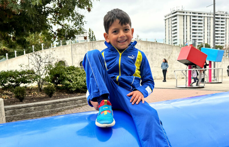 Simon is smiling and sitting on top of a large blue structure in what seems to be a park