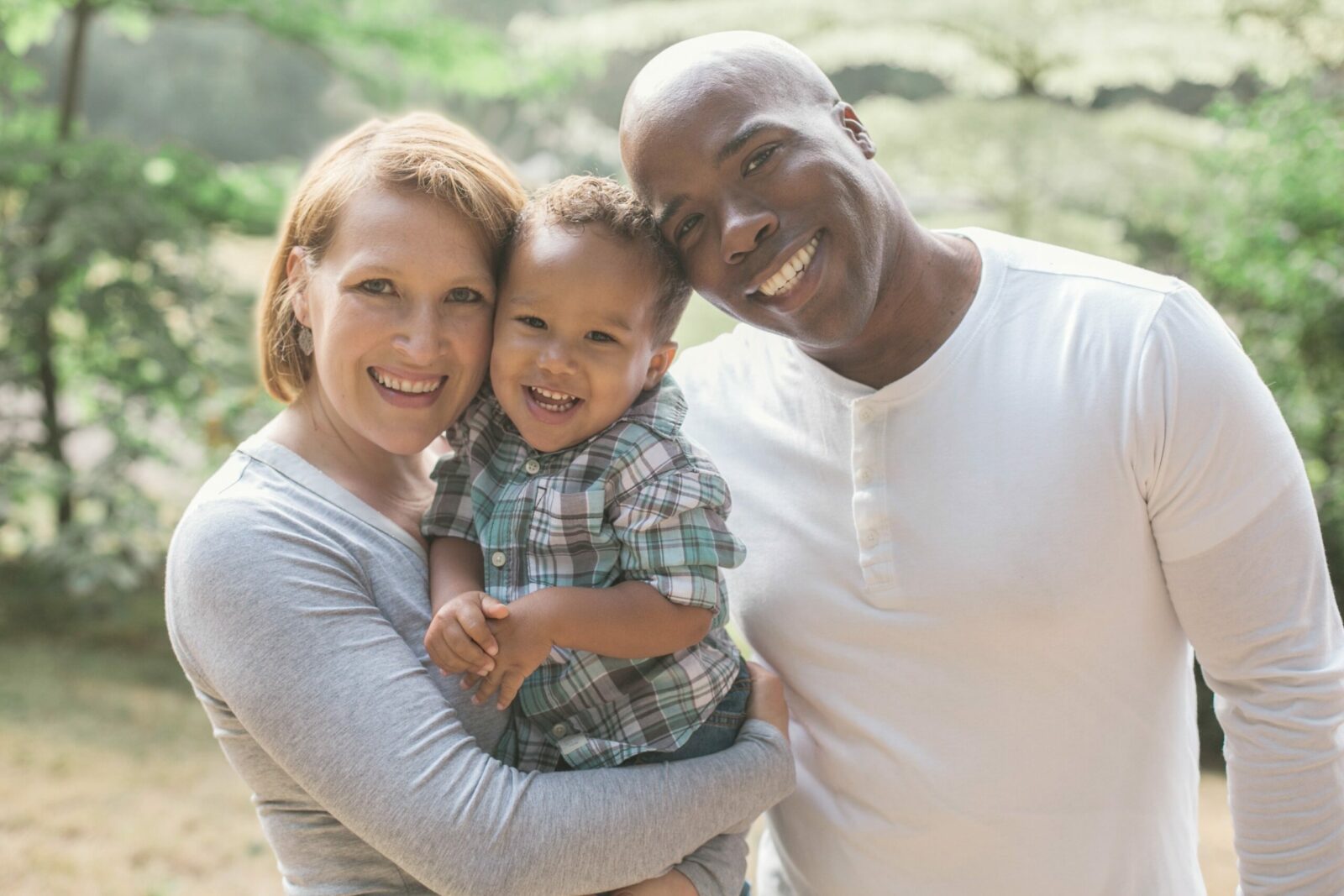 Woman, child and man outdoors, standing together and smiling.