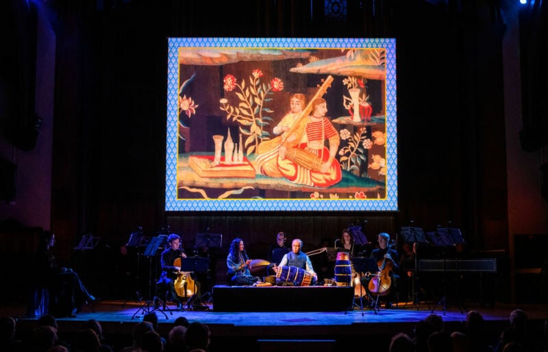 musicians are seating on stage; overhead is a project image of a baroque painting