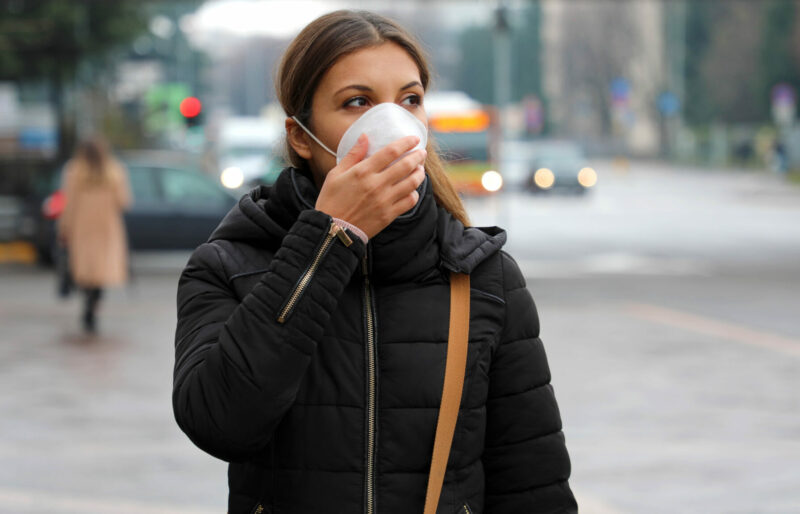 Young woman wearing a face mask walks down a city street