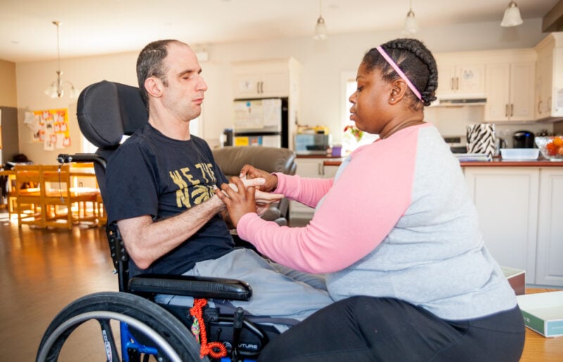 Man in a wheelchair is using sign language to communicate with his intervenor