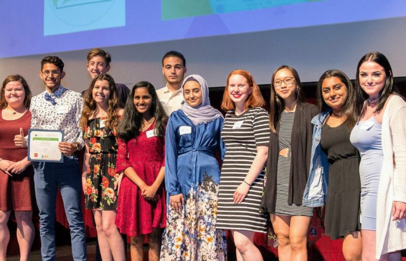 Group of diverse high school students standing on stage, looking at camera, smiling