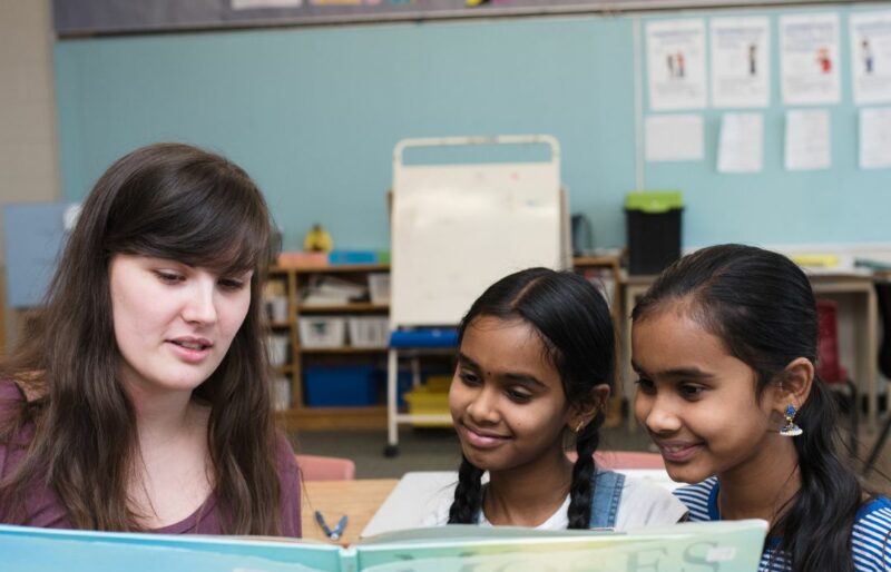 Woman sitting next to two young girls reading a picture book