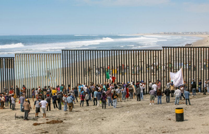 Dozens of migrants and workers on the sides of the US-Mexico border wall in Tijuana Beach.