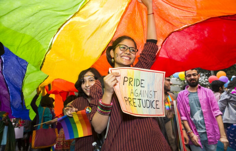 People stand under a large rainbow flag holding a sign that reads 'Pride against prejudice'