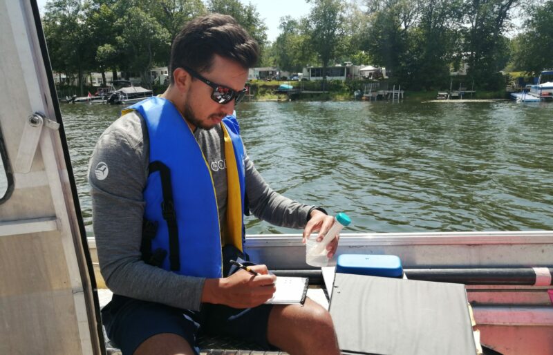 A man sits on a boat and collects water quality data.