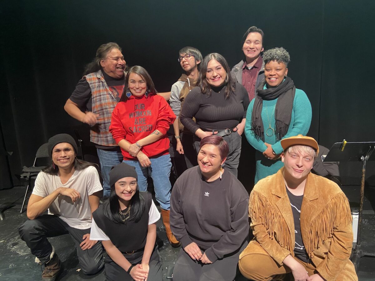 A group of people smiling and looking happy after the reading of CITY NDN LUV. Kneeling in the front row (left to right) are: Corvin Mack, Kaitlyn Yott, Kelsey Kanatan Wavey & Damion LeClair. Standing, staggered from left to right are: Sam Bob, Katie Manomie, Cameron Peal, Danica Charlie, Jeremy Ratt and Audrey Dwyer.