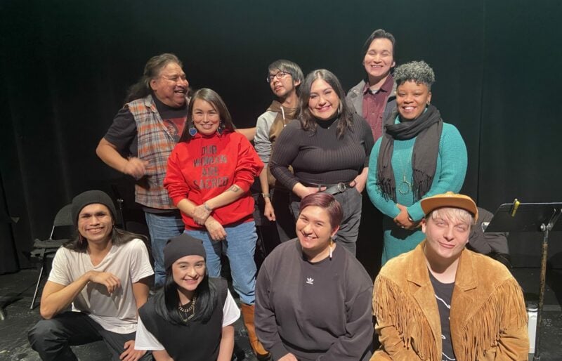A group of people smiling and looking happy after the reading of CITY NDN LUV. Kneeling in the front row (left to right) are: Corvin Mack, Kaitlyn Yott, Kelsey Kanatan Wavey & Damion LeClair. Standing, staggered from left to right are: Sam Bob, Katie Manomie, Cameron Peal, Danica Charlie, Jeremy Ratt and Audrey Dwyer.