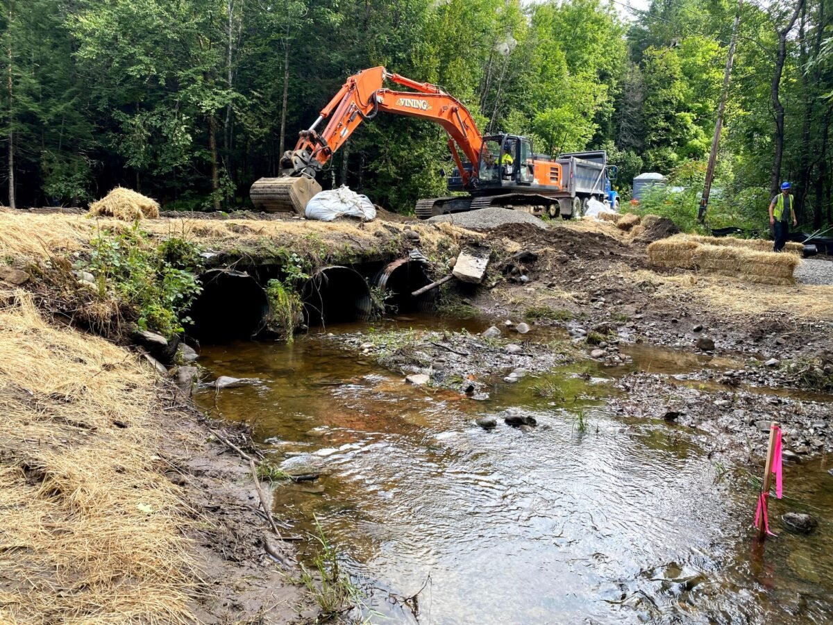 two collapsing culverts on a dirt road crossing with a stream flowing underneath