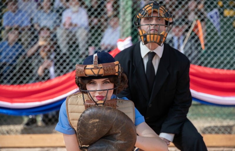 A female baseball catcher crouches in front of an umpire during a game.