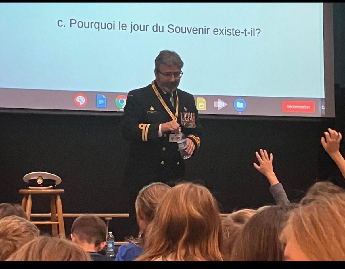 A uniformed officer standing in front of a screen speaks to a auditorium of students.