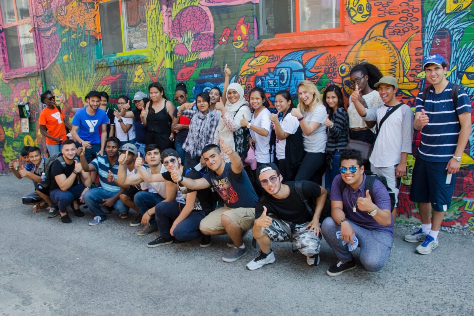 a gathering of diverse youth from the YMCA of Greater Toronto programs in front of a wall with graffiti