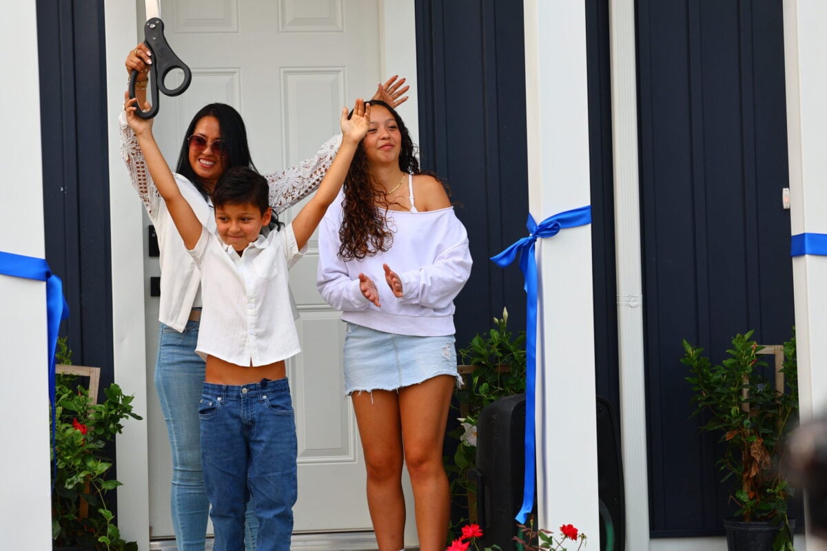 Family of three cutting the ribbon on the porch of their home