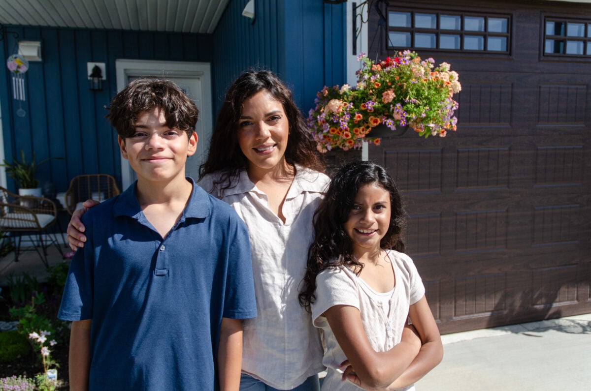 Family of three standing in the driveway in front of their home